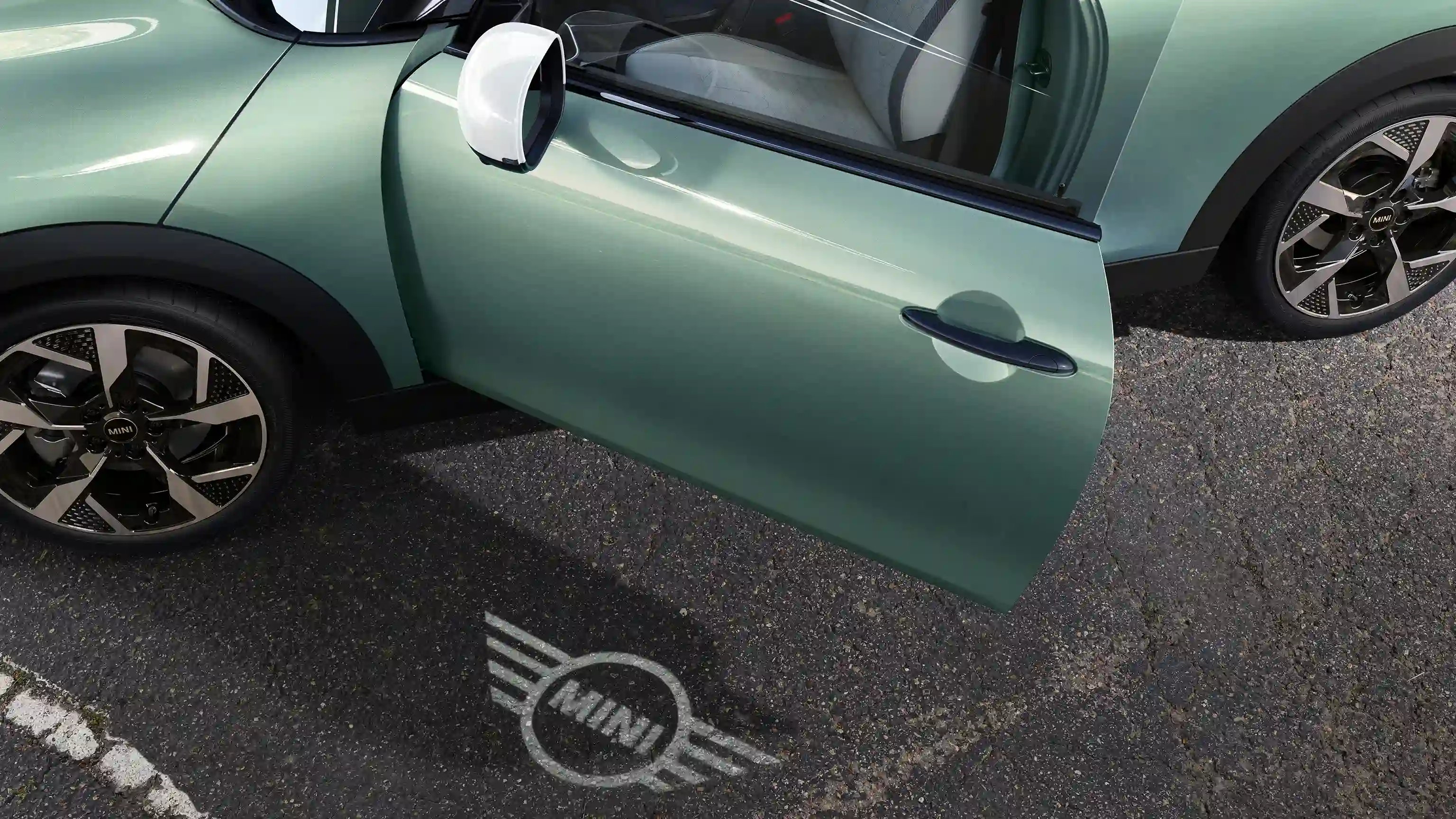 Exterior view of MINI Cooper with open door and MINI logo welcome light on the ground 