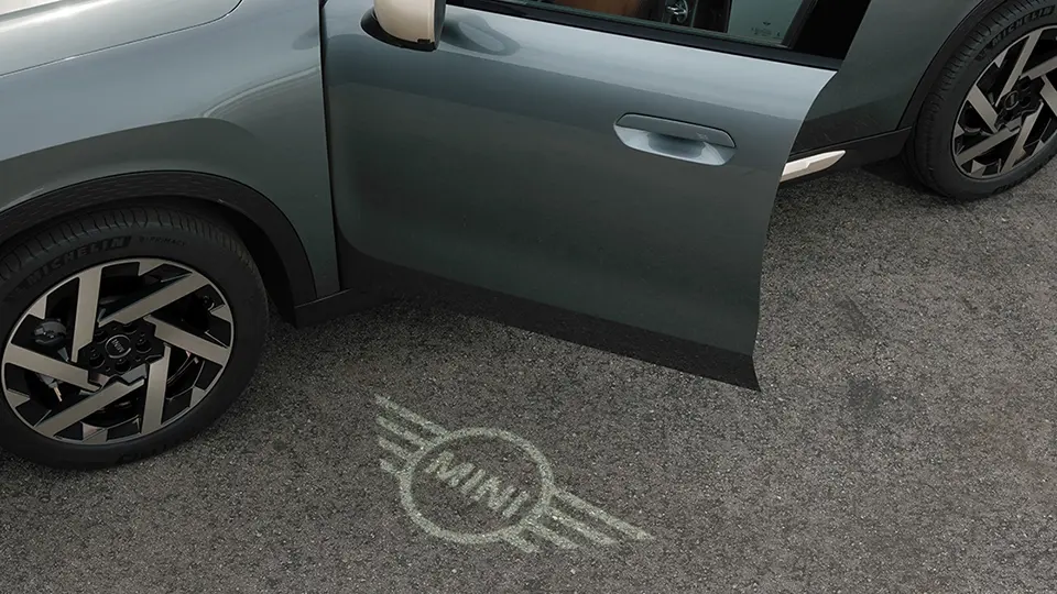 Exterior view of MINI Countryman with open door and MINI logo welcome light on the ground 