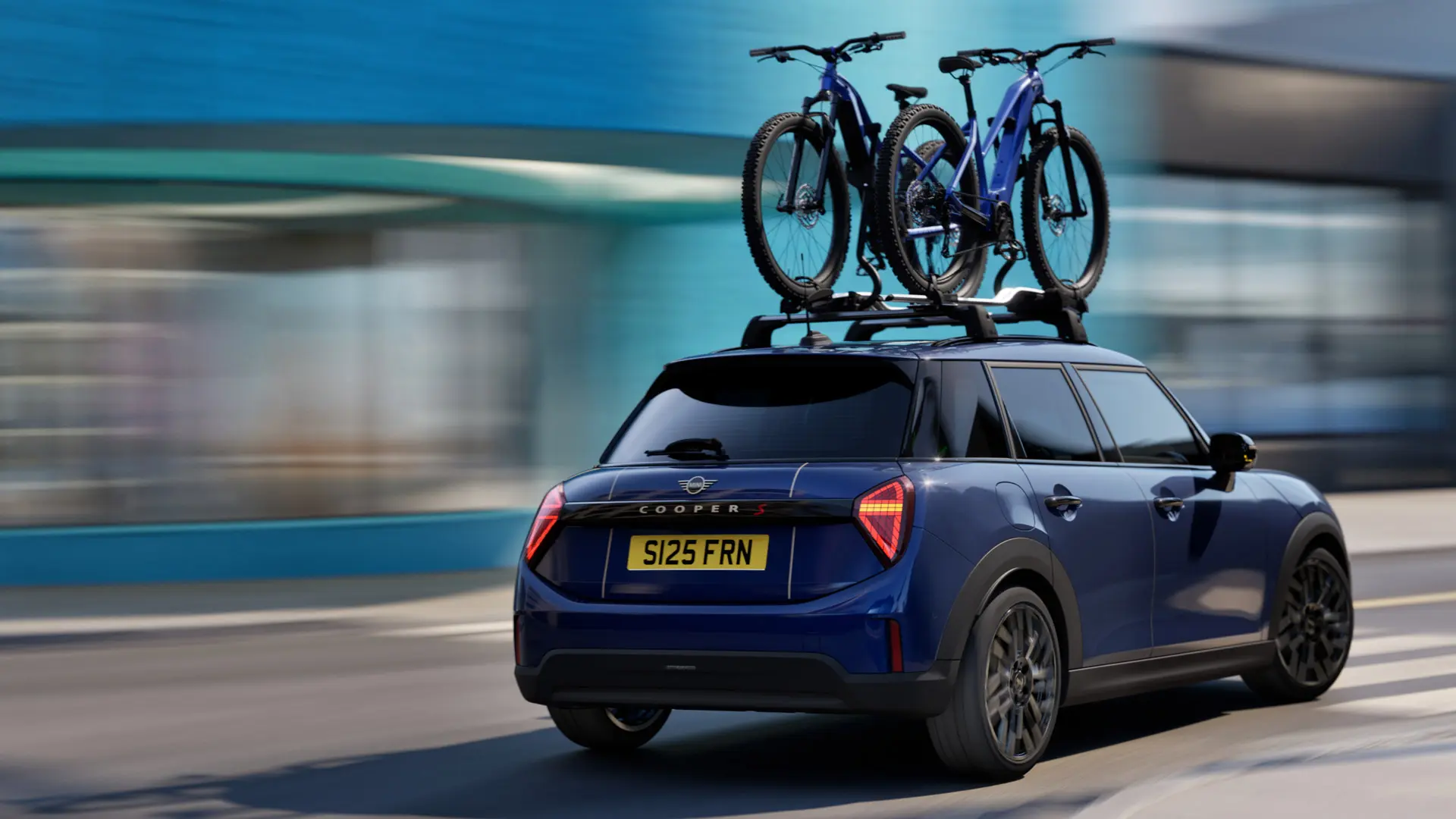 MINI Aceman in Indigo Sunset Blue equipped with MINI Roof Cycle Carrier, carrying two mountain bikes, three quarter rear view. 